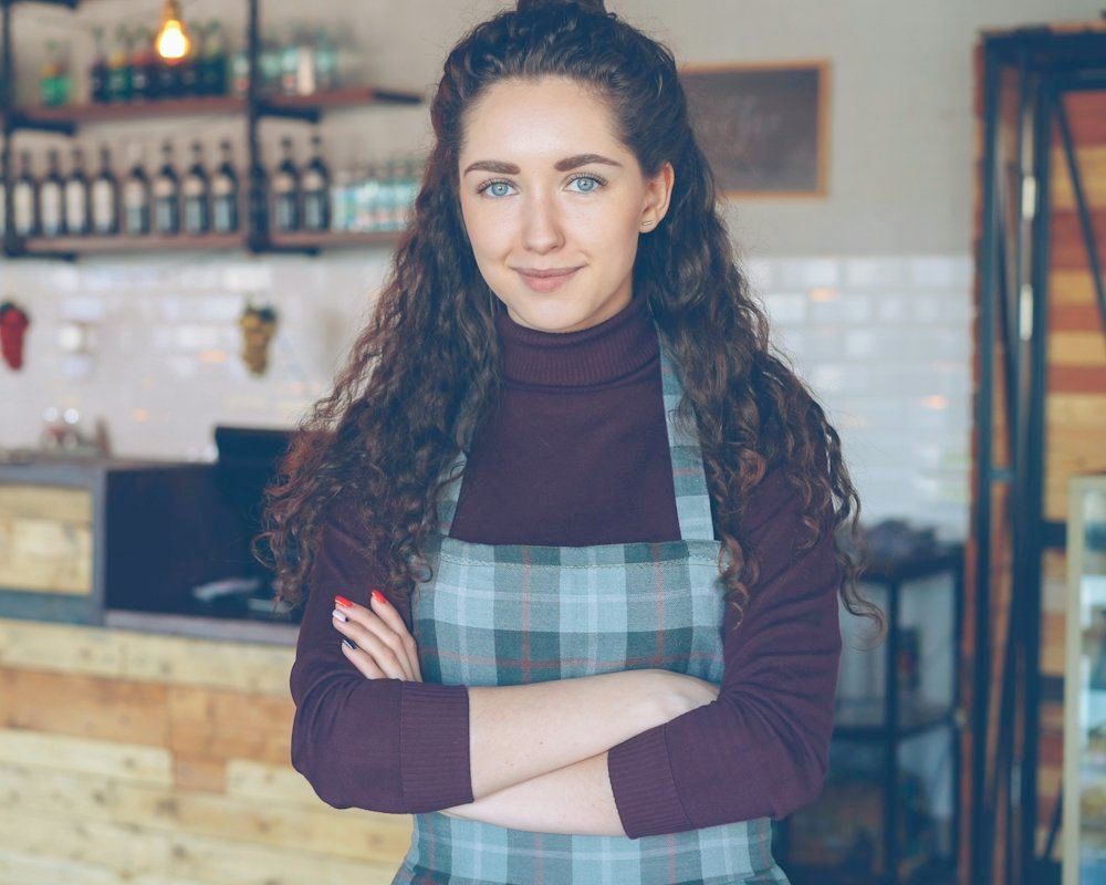 A café owner smiling with arms folded in her shop
